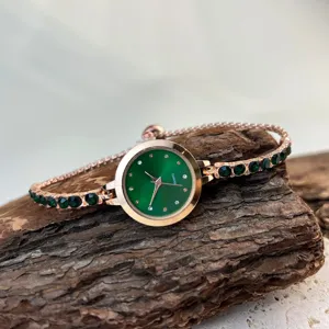 Detailed shot of a rose gold quartz women's watch with green dial and gemstone strap.