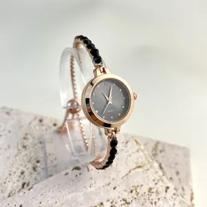Close-up detail of rose gold quartz watch, elegant black beaded bracelet strap on clear stand.