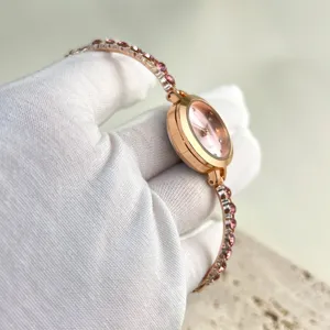 Close-up detail of a delicate rose gold women's quartz watch with sparkling pink crystal strap.