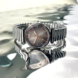 Primer plano de reloj de mujer con esfera gris y correa elastica de metal brillante.
