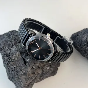 Detalle de primer plano de reloj de cuarzo para mujer con esfera negra y correa elástica.