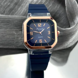 Detalle de reloj de cuarzo cuadrado, esfera azul con índices en oro rosa y correa de silicona azul.