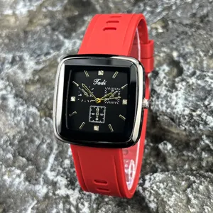 Quadratische Quarzuhr mit schwarzem Zifferblatt, goldenen Indizes und rotem Silikonarmband.