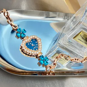 Elegant quartz bracelet watch featuring a heart dial, sparkling rhinestones, and blue clover charms.