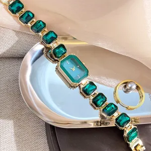 Detailaufnahme einer luxuriösen Smaragd-Quadratedelstein-Damenarmbanduhr mit goldenen Gliedern.