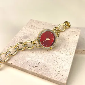 Nahaufnahme der goldenen Damenuhr mit rotem Zifferblatt und glitzernden Strasssteinen.