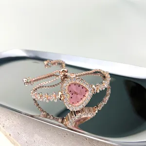 Nahaufnahme einer roségoldenen Herz-Quarzuhr mit funkelnden Strasssteinen und Blumenband.