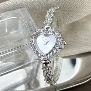 Nahaufnahme des silbernen Herz-Quarzuhrwerks mit glitzernden Strasssteinen und Blumenarmband.