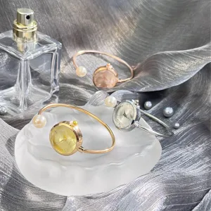 Detailansicht eleganter Perlen-Armreifuhren mit geometrisch geschliffenem Glas auf schickem grauen Satin.