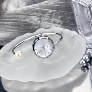 Nahaufnahme einer silbernen Armreif-Uhr mit Perle und glitzerndem Zifferblatt auf Ablage.