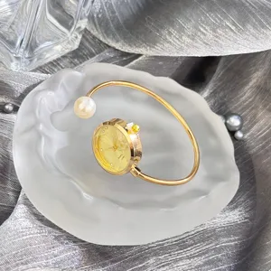 Detailaufnahme der eleganten goldenen Armreif-Uhr mit glänzender Perle und funkelndem Zifferblatt.