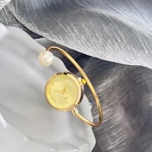Nahaufnahme der goldenen Armbanduhr mit Perle, facettiertem Zifferblatt und funkelnden Kristallen.
