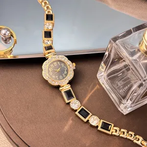 Gold tone bracelet watch featuring sparkling rhinestones, black square gems, and floral dial.