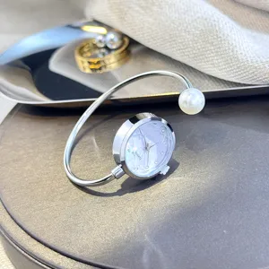 Nahaufnahme einer silbernen Armreif-Uhr mit facettiertem Glaszifferblatt und Perlendekor.