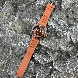 Detailaufnahme der braunen Silikonarmband Quarzuhr mit schwarzem Zifferblatt auf Stein.