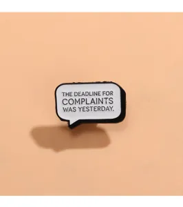 Close-up detail shot of the black and white speech bubble slogan metal brooch accessory.