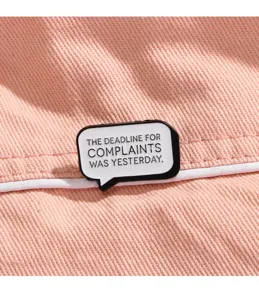 Close-up detail of a creative black and white slogan enamel brooch pin on pink denim.