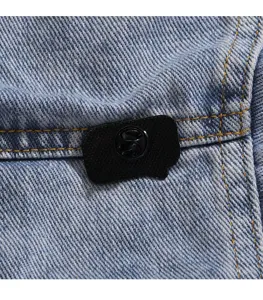 Detail of black enamel brooch pinned on blue denim fabric with yellow contrast stitching.