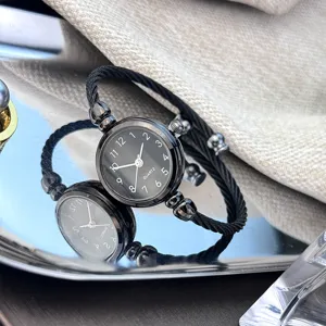Detailansicht einer minimalistischen Damenarmbanduhr mit schwarzem Zifferblatt und Drahtarmband.