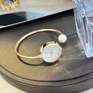Elegante goldene Armreif-Uhr mit zarter Perle und funkelnden Kristall-Zifferblattmarkierungen.