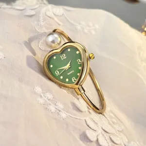 Nahaufnahme der eleganten herzförmigen grünen Zifferblattuhr mit Perlenarmreif und Gold-Finish.