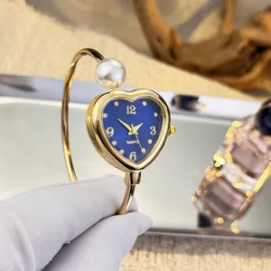 Nahaufnahme der eleganten goldenen Herz-Armreif-Uhr mit Perlenakzent und blauem Zifferblatt.