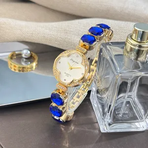 Reloj de cuarzo para mujer con eslabones de trébol azul, correa dorada y elegante caja.