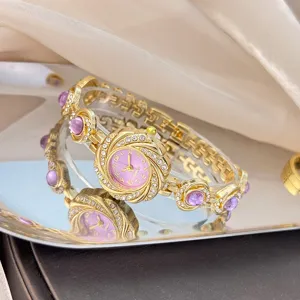 Goldfarbene Strass Quarz Armbanduhr für Damen mit rosafarbenem Zifferblatt und Schmuck.