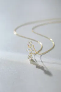 Detailed shot of triple four-leaf clover pendant necklace with sparkling stones in fine gold finish.