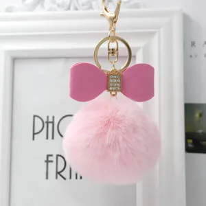 Close-up of fluffy pink faux fur pom pom keychain with cute bow and gold hardware accessory.