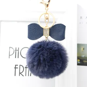 Dark blue faux fur pom pom keychain with leather bow and sparkling rhinestone decor.