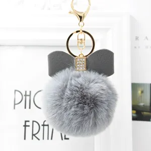 Grey faux fur pom pom keychain detail featuring a leather bow and metal hardware clasp.