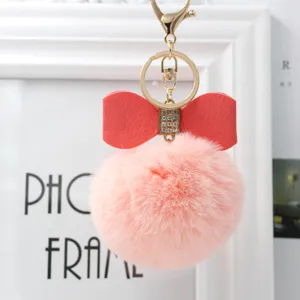 Fluffy pink pom pom keychain with red leather bow and gold hardware for bags and keys.