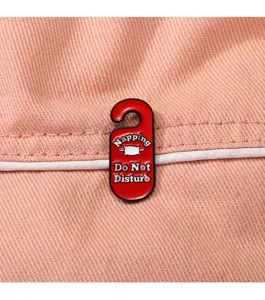 Vista dettagliata di una spilla in metallo smaltato rosso con design da appendiabiti e testo.