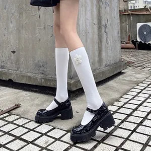 Detail view of white mid-calf socks with delicate pearl flower decor paired with black shoes.