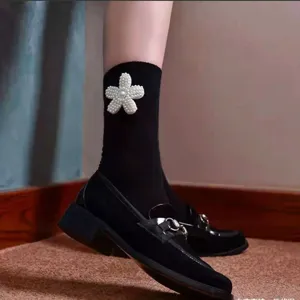 Close-up detail of black calf socks featuring elegant white pearl flower decoration.