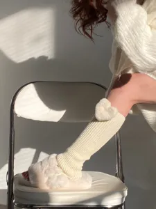 Detailed shot of cozy knit leg warmers featuring fluffy heart decor for winter style.