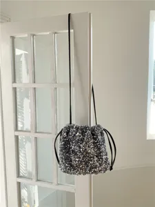 Vue détaillée d'un sac seau scintillant à sequins avec des cordons noirs élégants.