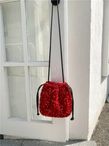Détail de sac seau à sequins rouges avec finition brillante, fermeture à cordon et lanière.