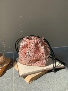 Vue détail du sac seau à cordon en paillettes roses montrant sa texture douce au soleil.