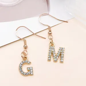 Primo piano di orecchini pendenti con lettere strass G e M in finitura oro KC.