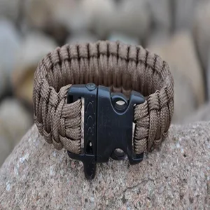 Close-up of brown paracord survival bracelet with black whistle buckle on natural stone background.