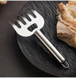 Close up view of stainless steel meat shredder fork on dark plate with cooked sliced meat.