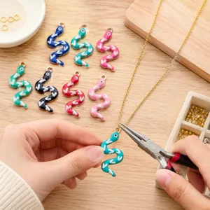 Detailed shot of DIY colorful snake enamel pendants and jewelry making tools on wooden table.