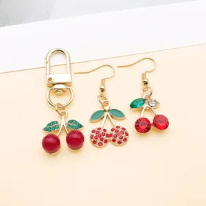 Gold-tone alloy cherry charm and earrings set with red and green crystal rhinestones.