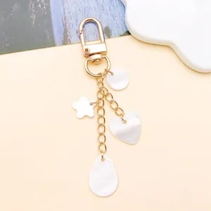 Dettaglio ciondolo DIY in conchiglia bianca con chiusura e forme in madreperla come stella e cuore.
