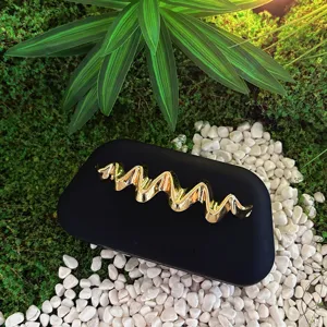 Detailed view of black matte clutch bag with luxury golden wavy metal decoration in natural scene.