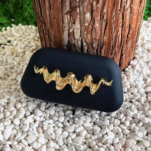 Detail view highlighting the metallic gold wave decoration on the black matte evening clutch surface.