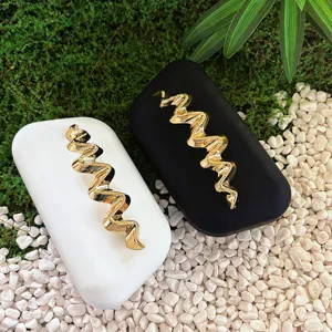 Close-up detail of frosted black and white clutch bags featuring elegant gold wave metal decor.