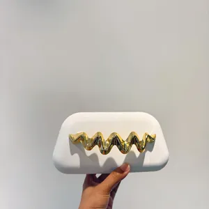 Detail shot of a white matte clutch bag featuring an elegant gold wavy metal decoration.